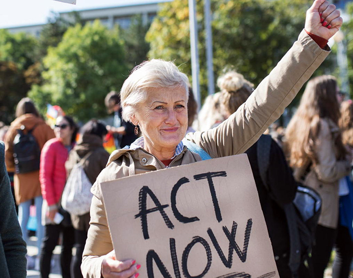 senior woman carries an "act now" sign during a protest