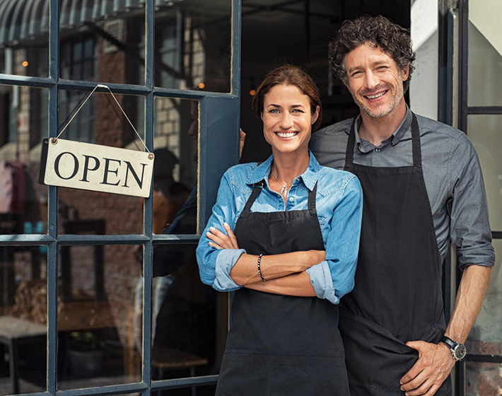 older couple as small business owners stand in front of their open store