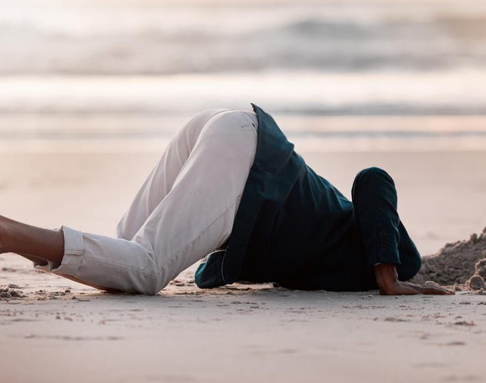 a person kneels on the sand with their head in a hole as they dig for buried treasure, a metaphor for cleaning a CRM