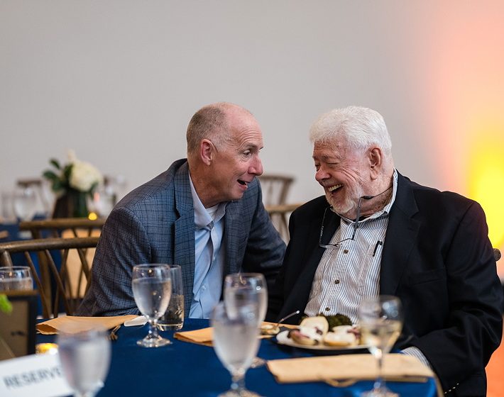 a professional photograph of two senior men laughing over lunch