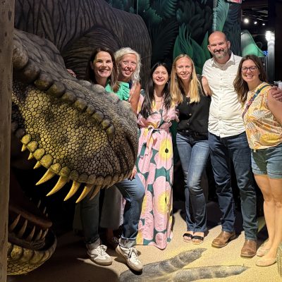 Maribeth, Angela, Karla, Rebecca, Jeff, and Natalie pose next to a giant T-Rex dinosaur at mini golf